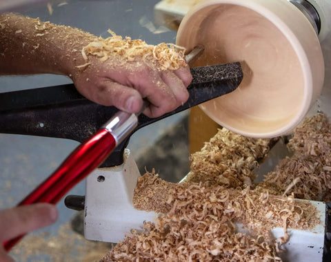 Carbide wood turning tool with a red aluminum handle on a wood lathe amid wood shavings
