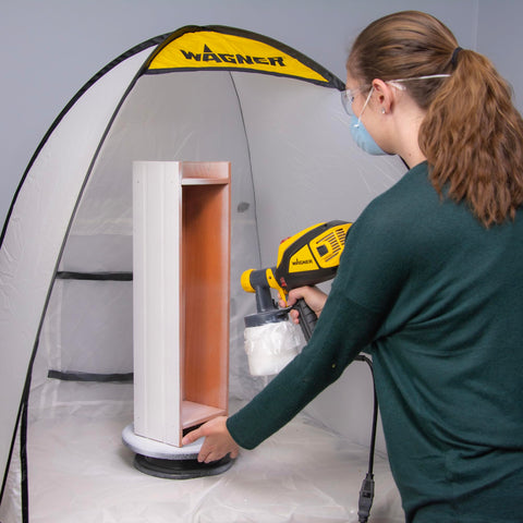 Woman using a spray gun inside a tent with a Revolving Paint Spray Turntable With 11 Inch Round Platform For Spray Painting Projects And Crafting Smooth 360 Degree Rotation For Accessing Every Angle On Miniatures Lamps Bird Houses Models And More.