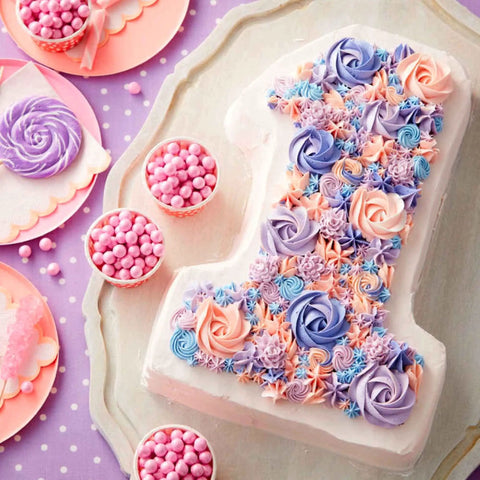 Number one cake decorated with pink, purple, and blue icing rosettes, surrounded by pink candies and a lollipop on a tray