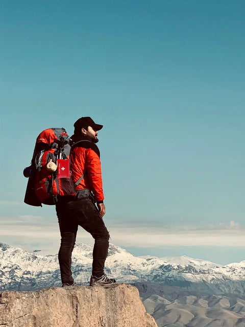 Small red 97-piece travel first aid kit attached to a hiking backpack on a mountain overlook.