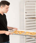 Person holding Pro Grade Aluminum Baking Sheet Pan For Oven 18 Inch Long By 26 Inch Wide By 1 Inch Deep Cookie Sheet 12 Pack with cookies.