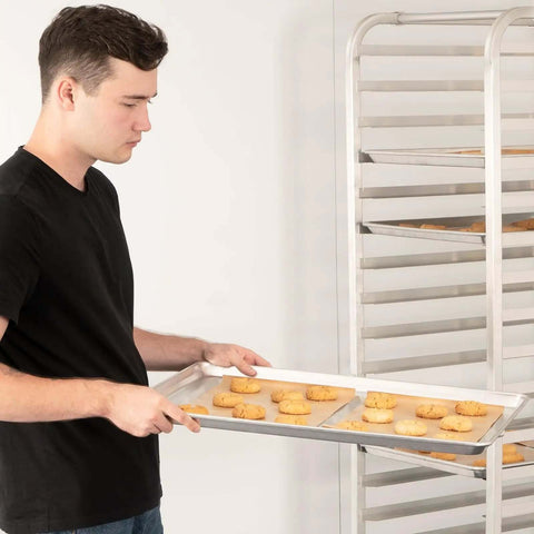 Person holding Pro Grade Aluminum Baking Sheet Pan For Oven 18 Inch Long By 26 Inch Wide By 1 Inch Deep Cookie Sheet 12 Pack with cookies.