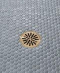 Smooth Draining Four Inch Round Shower Floor Drain With Removable Grate And Solid Gasket For Zero Fuss Tile Installation Featuring Fast Height Adjustment Plus Warm Brushed Gold Finish installed in light grey pebble tile.