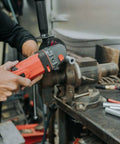 Person using a power tool to cut a round aluminum spacer on a workbench with other tools nearby.
