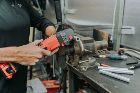 Person using a power tool to cut a round aluminum spacer on a workbench with other tools nearby.