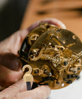 Hands holding clock mechanism with Vintage Grandpa Clock Repair Weight Kit With Shell Hook And Nut Replacement shown in foreground.