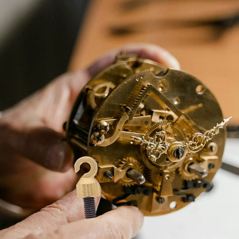 Hands holding clock mechanism with Vintage Grandpa Clock Repair Weight Kit With Shell Hook And Nut Replacement shown in foreground.