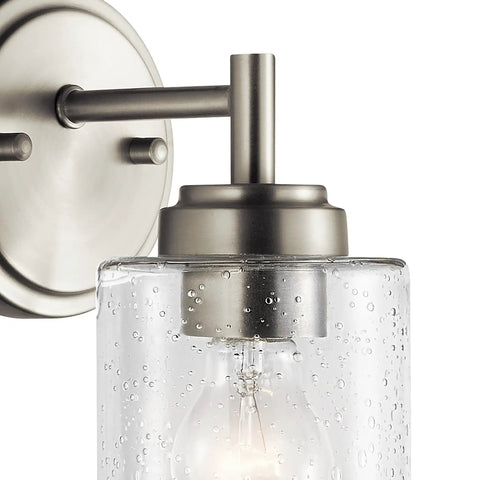 Close-up of Winslow 9.25 Inch Wall Sconce in Brushed Nickel with Clear Seeded Glass showing light bulb and mounting detail.