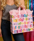Person holding 13 Inch Pink Happy Birthday Gift Bag With Colorful Lettering Design Card Tissue Paper And Sturdy Handles For Kids And Adults