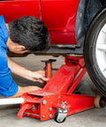Mechanic using heavy duty floor jack with casters replacement parts in garage, supporting car for maintenance