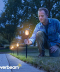 Man installing P2 Solar Flickering Flame Torch Light With Realistic Fire, IP65 Waterproof Outdoor Tiki Lamp, in a garden.