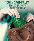 Front view: Purelid eyelid wipes sachet with tea tree oil, green package being placed into a brown handbag