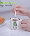 Hand stirring coffee in a ceramic mug with cactus design on a table with a napkin.