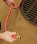 Person holding Heavy Duty Three Quarter Inch Water Hose 100 Foot, Workhorse Rubber and Vinyl with Rugged Red Cover, near drain
