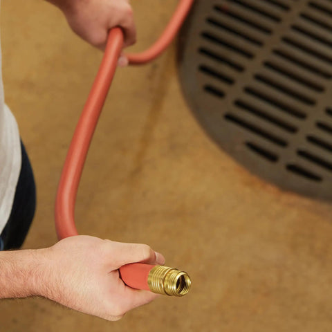 Person holding Heavy Duty Three Quarter Inch Water Hose 100 Foot, Workhorse Rubber and Vinyl with Rugged Red Cover, near drain