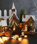 Miniature village with snow-covered houses, pine cones, and decorative lights creating a festive scene on a dark background.