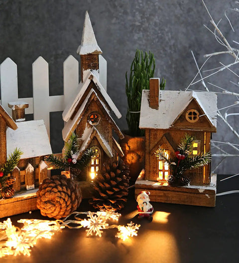 Miniature village with snow-covered houses, pine cones, and decorative lights creating a festive scene on a dark background.