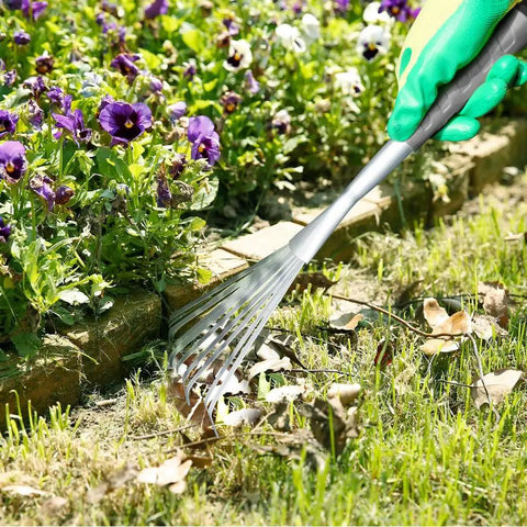 Person using Adjustable 17 To 63 Inch Thatch Rake With 24 Steel Tines for garden cleanup of leaves and debris near flowers.
