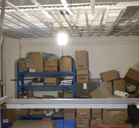 100W LED Tripod Work Light With Stand illuminating a garage with boxes and metal shelving, 14000 Lumen Corded Jobsite Light
