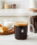 Two Pack Beaker Mugs With Handles, 16 Oz Caffeine Molecule Glass Coffee Cups on table with coffee beans and pastries