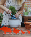 Four orange animal silhouette steel targets on a table in garden setting, featuring boar, duck, bird, and rat designs.