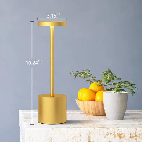 Side view of Two Pack Cordless Table Lamp Set with 5000mAh Rechargeable Battery, gold finish, on a table with fruit bowl and plant.