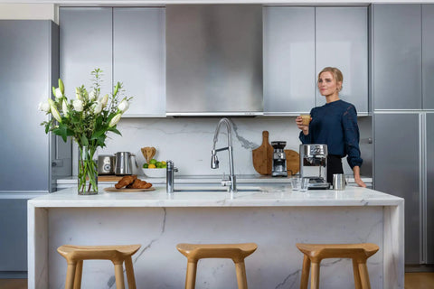 Woman in kitchen with Bambino Plus Espresso Machine for Home Baristas with Dose Control and Auto Milk Frother on countertop