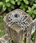 Chain Link Gate Latch with Double Carabiner Ends Stainless Steel coiled on a wooden post outdoors with greenery background.