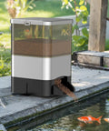 No Sweat Automatic Fish Feeder For Koi Ponds featuring large 10l tank dispensing pellets into pond with visible fish.
