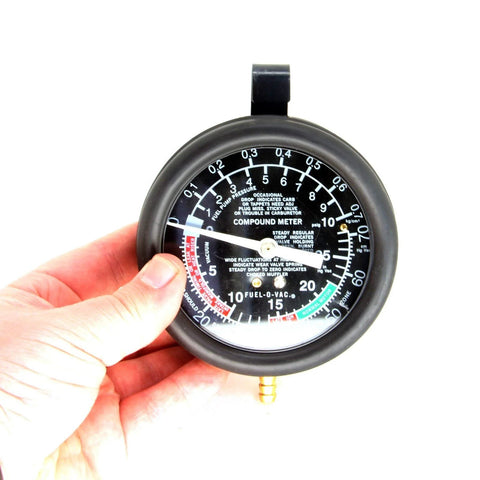 Front view of handheld HFS fuel pump tester gauge; black round dial with white markings and brass bottom connector.