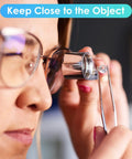 Close-up of person using 40X Jewelers Loupe Magnifier Pro Grade With LED And UV Illumination examining a small object with tweezers.
