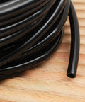 Coiled Heavy Duty Garden Drip Irrigation Hose For Greenhouse And Lawn, black PVC one quarter inch tubing on wooden surface