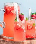 Three glasses of strawberry lemonade with glass straws, garnished with strawberries and mint, on a wooden tray.