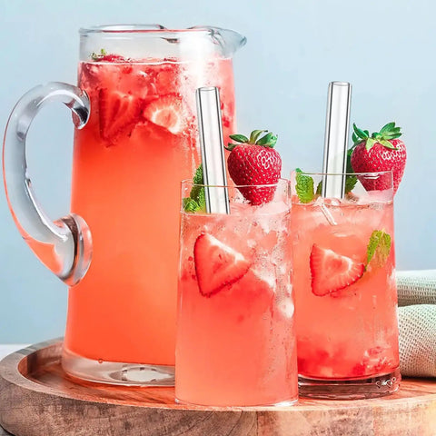 Three glasses of strawberry lemonade with glass straws, garnished with strawberries and mint, on a wooden tray.