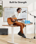 Huanuo Electric Standing Desk Frame With Powerful Brushless Motor For Dual Monitor Riser, man playing guitar, supports loads up to 220 lbs.