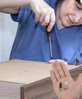 Person assembling cabinet using 24 Piece Furniture Connector Hardware Kit for Cabinet and Wardrobe Assembly, visible on hand.