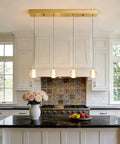 Modern kitchen with pendant lights above a marble island, featuring a vase of roses and a colorful tile backsplash in natural light.