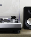Crosley C100A Silver Belt Drive Turntable With Aluminum Tonearm Pitch Control For 33 And 45 Rpm Vinyl Records and speaker setup.