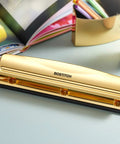 Gold 3 Hole Punch For 12 Sheets Durable Metal Office Punch With Stable Rubber Base on a desk with books and plant