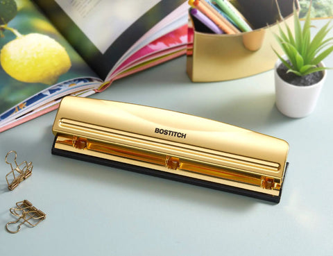 Gold 3 Hole Punch For 12 Sheets Durable Metal Office Punch With Stable Rubber Base on a desk with books and plant