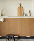 Kitchen setting with Adhesive Touchless Foot Pull for Cabinet Trash Cans, Silvery Finish, visible under wooden overlay cabinet doors.