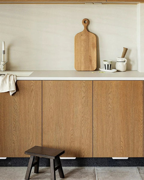 Kitchen setting with Adhesive Touchless Foot Pull for Cabinet Trash Cans, Silvery Finish, visible under wooden overlay cabinet doors.