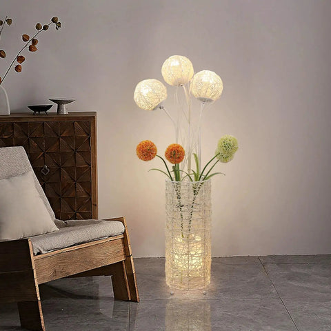 Pastoral LED Floor Lamp With Handwoven Rattan Flower Shade casting warm light beside a wooden chair in a cozy room setting