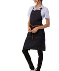 Person wearing Unisex Memphis Bib Apron In Indigo Blue With Adjustable Neck Buckle And Waist Ties, front view, casual setting.