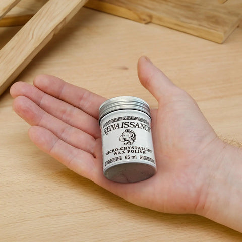 Hand holding 65 ml tin of Micro Crystalline Wax Polish For Furniture, Wood, Leather And Metal That Delivers A Slick Shine