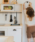 Child reaching in play kitchen with black T Bar handles on cabinets and drawers, modern cupboard hardware visible.