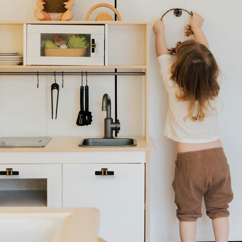 Child reaching in play kitchen with black T Bar handles on cabinets and drawers, modern cupboard hardware visible.