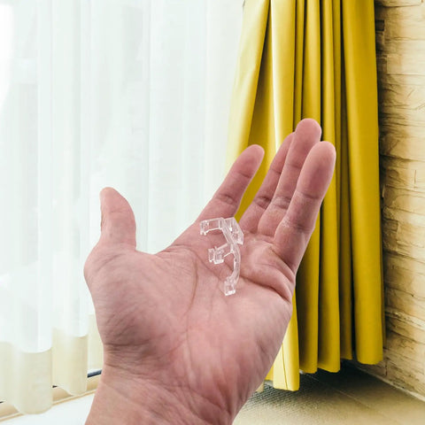 Premium Clear Double Slat Valance Clips To Tuck Away Mini Blind Brackets in hand, sturdy plastic, two inches wide.