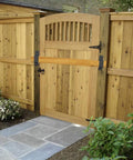 Wooden garden gate with arched top, situated within a wooden fence, surrounded by stone pathway and greenery.
