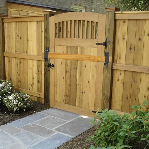 Wooden garden gate with arched top, situated within a wooden fence, surrounded by stone pathway and greenery.